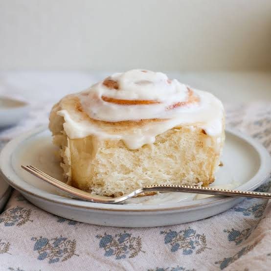 Hand pulling a fresh cinnamon roll from the pan